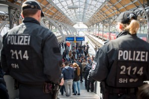 Policemen look at a group of refugees waiting on a platform of the main station in Luebeck, northern Germany, on September 8, 2015, after police stopped a train carrying migrants heading to Denmark due to a lack of visas.   AFP PHOTO / DPA / DANIEL REINHARDT  GERMANY OUT